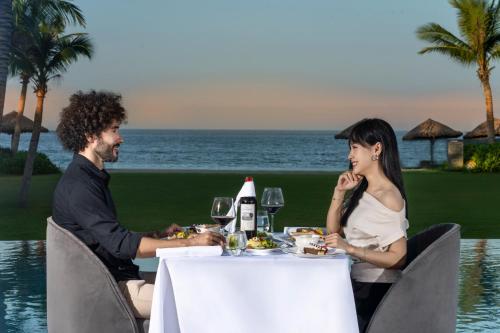 a man and a woman sitting at a table with food at Hoi An Royal Beachfront Villas in Dien Ban