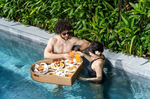 a man and a woman sitting in a pool with a tray of food at Hoi An Royal Beachfront Villas in Dien Ban