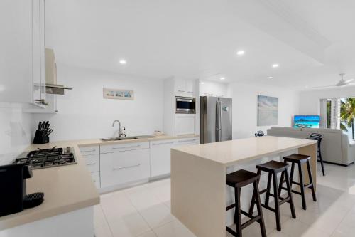 a kitchen with white cabinets and a island with bar stools at Rojo at Island Views—A Breezy Beachfront Retreat in Palm Cove