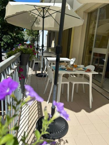 a table with an umbrella on a balcony with purple flowers at Hotel De La Ville in Rimini