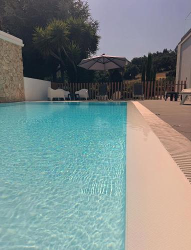 a blue swimming pool with chairs and an umbrella at 3M Hostel & Suites in Alvaiázere