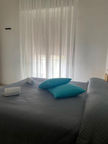 a bed with two blue pillows and a window at Hotel De La Ville in Rimini