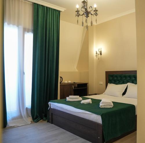 a bedroom with a bed with green curtains and a chandelier at Hotel BABU in Kutaisi