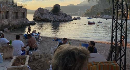 a group of people sitting on a beach near the water at Studio Sea View Steps to Przno beach w Parking Villa Olive in Pržno