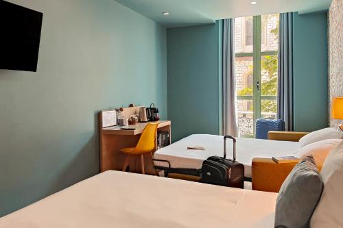 a room with two beds and a desk and a window at Hôtel Du Centre, un hôtel AMMI in Nice