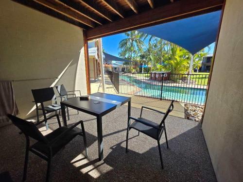 Un patio con mesa y sillas y una piscina. en Palm Breeze Holiday Unit, en Agnes Water
