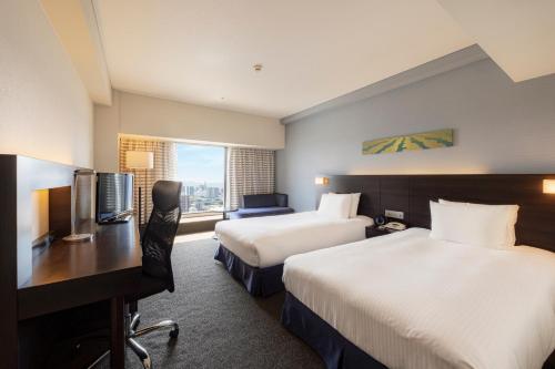 a hotel room with two beds and a desk at ANA Crowne Plaza Kumamoto New Sky by IHG in Kumamoto