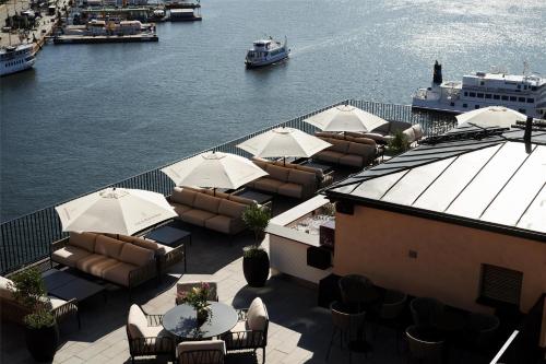 a patio with tables and chairs and a boat in the water at Radisson Collection, Strand Hotel, Stockholm in Stockholm