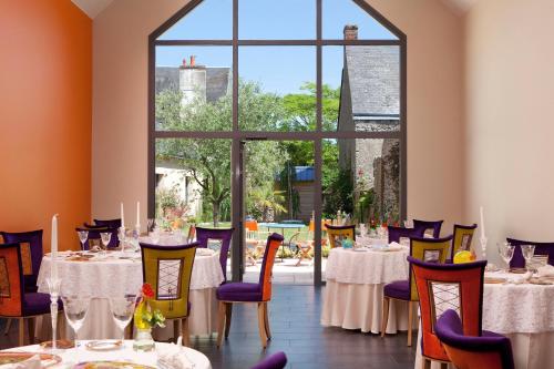 een eetkamer met tafels en stoelen en een groot raam bij Logis hôtel Ô en Couleur in Oucques