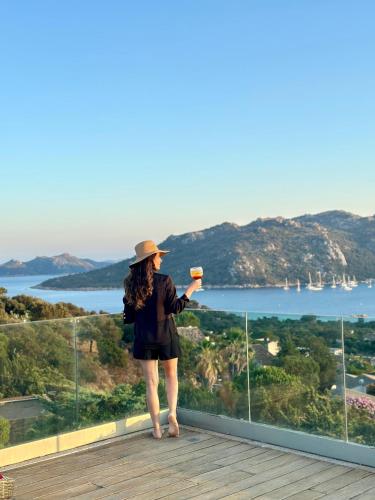 a woman standing on a balcony holding a drink at Hotel Carre Noir in Porto-Vecchio