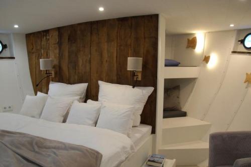 ein Schlafzimmer mit einem Bett mit weißen Kissen und einer Treppe in der Unterkunft 8 Personen Hausboot mit Hot Tub, Sauna, Kaminofen, Klimaanlage, Lounge, Sonnendeck und Garten mit Buddelschiff direkt hinterm Deich in Otterndorf in Otterndorf