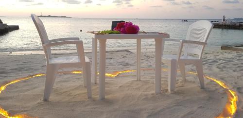 a table and chairs on the beach with a bouquet of flowers at Garden Rooms by Lagoon View in Bodufolhudhoo