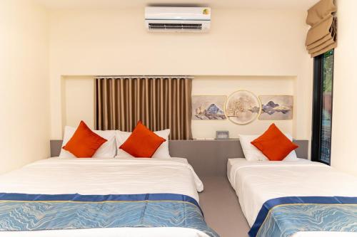 two beds in a hotel room with orange pillows at The Swan Pool Villa Hatyai เดอะสวอน พูลวิลล่าหาดใหญ่ in Ban Kohong
