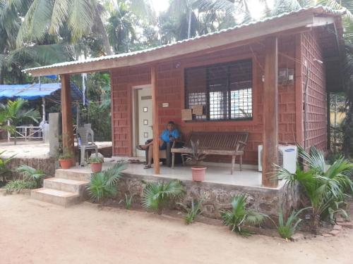 a woman sitting on a bench outside of a house at Tendulkar Beach Resort in Diveagar