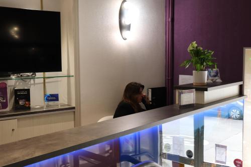 a woman sitting at a counter in a hotel room at The Originals City - Hôtel Saint-Martial, Limoges Centre in Limoges