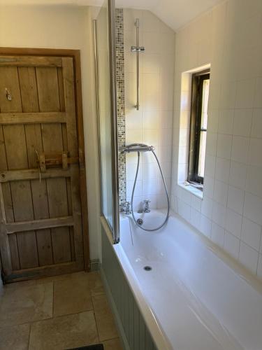 a bathroom with a tub and a window and a door at The Barn, Higher Boden, Manaccan, Helston, Cornwall in Helston