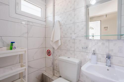 a white bathroom with a toilet and a sink at Seaview Tranquility - Elegant Escapes by the Shore in Ayía Kiriakí