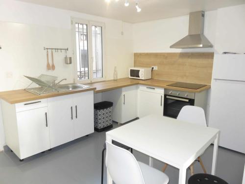 une cuisine avec des placards blancs et une table et des chaises blanches dans l'établissement Le 14 - 1 Chambre hyper centre, à Béziers