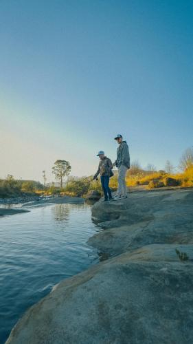 two people are standing on rocks near a river at Gooderson Drakensberg Gardens Golf & Spa Resort in Drakensberg Garden