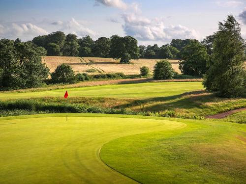 a lush green golf course with a red flag on a green field at Macdonald Portal Hotel, Spa & Golf Resort in Tarporley