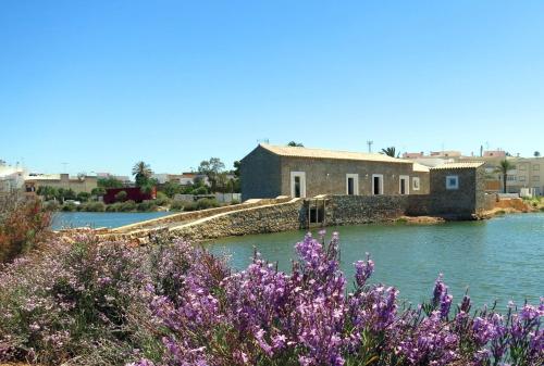 a building in the middle of a lake with purple flowers at Moinhos das Marés in Fuzeta