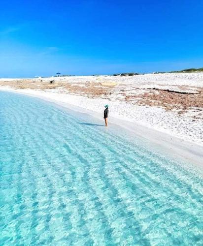 a person standing on a beach with blue water at Domos Sa Murta in Solanas