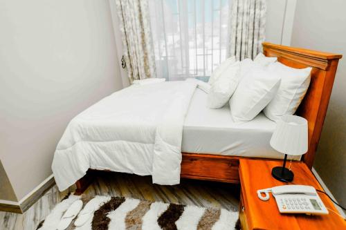 a bed with white sheets and a phone on a table at Joy Inn Hotel in Dar es Salaam
