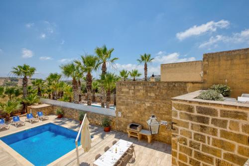 a patio with a swimming pool and palm trees at Karmnu Holiday Farmhouse in Għasri