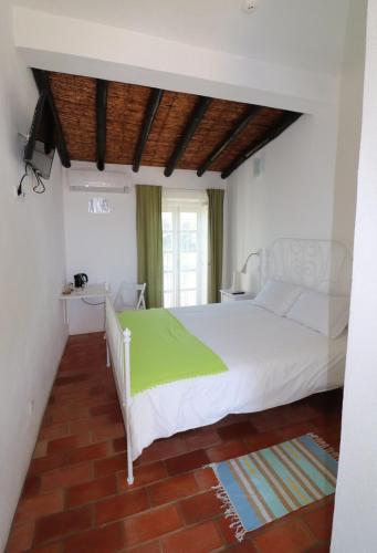 a bedroom with a white bed with a green blanket at Moinhos das Marés in Fuzeta
