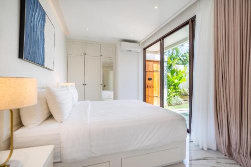 a white bedroom with a bed and a sliding glass door at Frelin Villas - 1 BR, 2 BR Luxury Villa Complex in Kerobokan