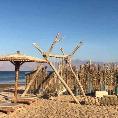 a wooden structure on a beach with an umbrella at Ciao Hotel in Nuweiba