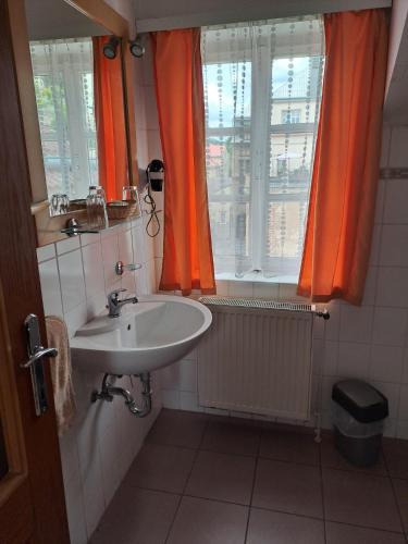 a bathroom with a sink and a window with orange curtains at Penzion Andy in Děčín