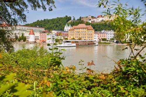 a river with buildings and a boat in the water at Hotel Innsento - Health Campus Passau in Passau