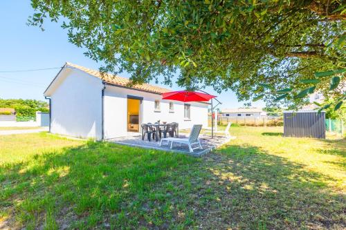 a small white house with a table and a red umbrella at Gemma - 5 min de la Plage in Ondres