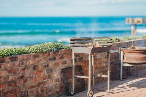 a barbecue grill next to a brick wall next to the ocean at Silver Spray Beach Accommodation in Victoria Bay