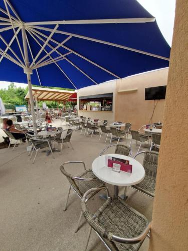 a group of tables and chairs with a blue umbrella at Mobil home en Provence - Camping 4 étoiles- 2 chambres -4 à 6 pers-clim-terrasse-TV in Cadenet