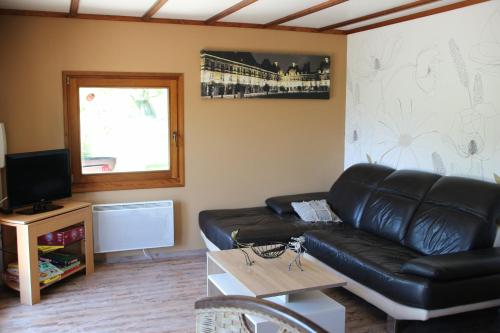 a living room with a black leather couch and a television at Chalet du Lièvre in Hannappes