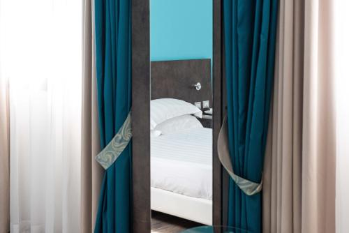 a mirror in front of a bed with blue curtains at Phi Hotel Milano in Baranzate