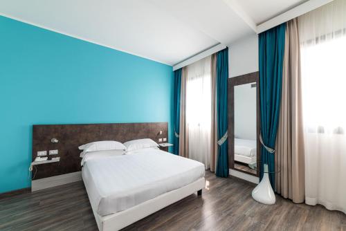 a bedroom with a white bed and a blue wall at Phi Hotel Milano in Baranzate