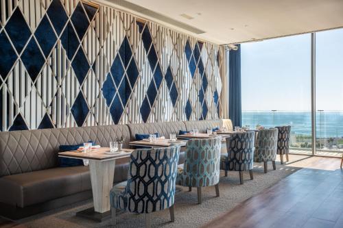 Un restaurante con mesas y sillas y un gran ventanal. en Leonardo Royal Hotel Barcelona Forum, en Barcelona