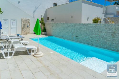 a pool with chairs and a table and a green umbrella at Villa Mediterranea Apartments - Seaview, Pool & Garden in Bari