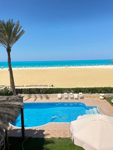 a swimming pool next to a beach with a palm tree at فيلا اول صف بحر مارينا الساحل الشمالي العلمين برايفت بول in El Alamein