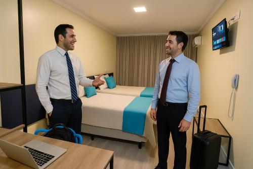 two men standing in a room with a bed at Hotel Suntuoso in Brasilia