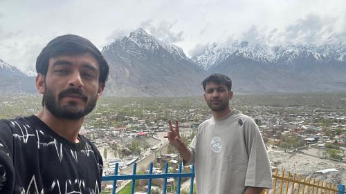 two men standing in front of a city with mountains at Skardu Baltistan Village Guest House in Skardu