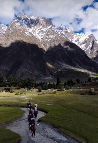 a group of people riding horses through a river with a mountain at Skardu Baltistan Village Guest House in Skardu