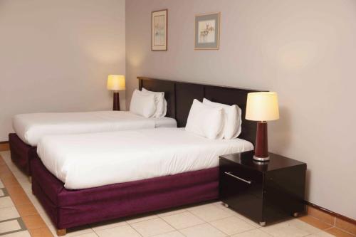 two beds in a hotel room with a lamp on a night stand at Safari Lodge in Windhoek
