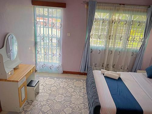 a bedroom with a bed and a vanity and two windows at Homely apartments 4 in Kisumu