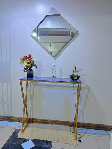a table with a mirror and a vase with flowers on it at Homely apartments 4 in Kisumu