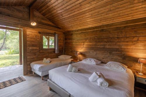 two beds in a room with wooden walls at Les Lodges du Lac in Saint-Alban-de-Montbel