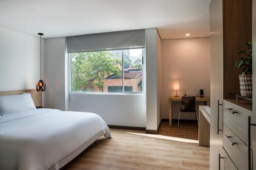 a bedroom with a white bed and a large window at Hotel Poblado Alejandria in Medellín